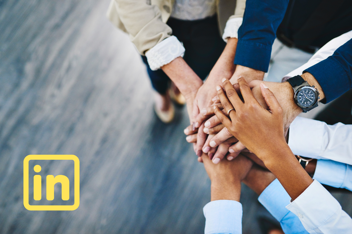 5 people in an office putting their hands together, with a LinkedIn logo in the bottom left corner